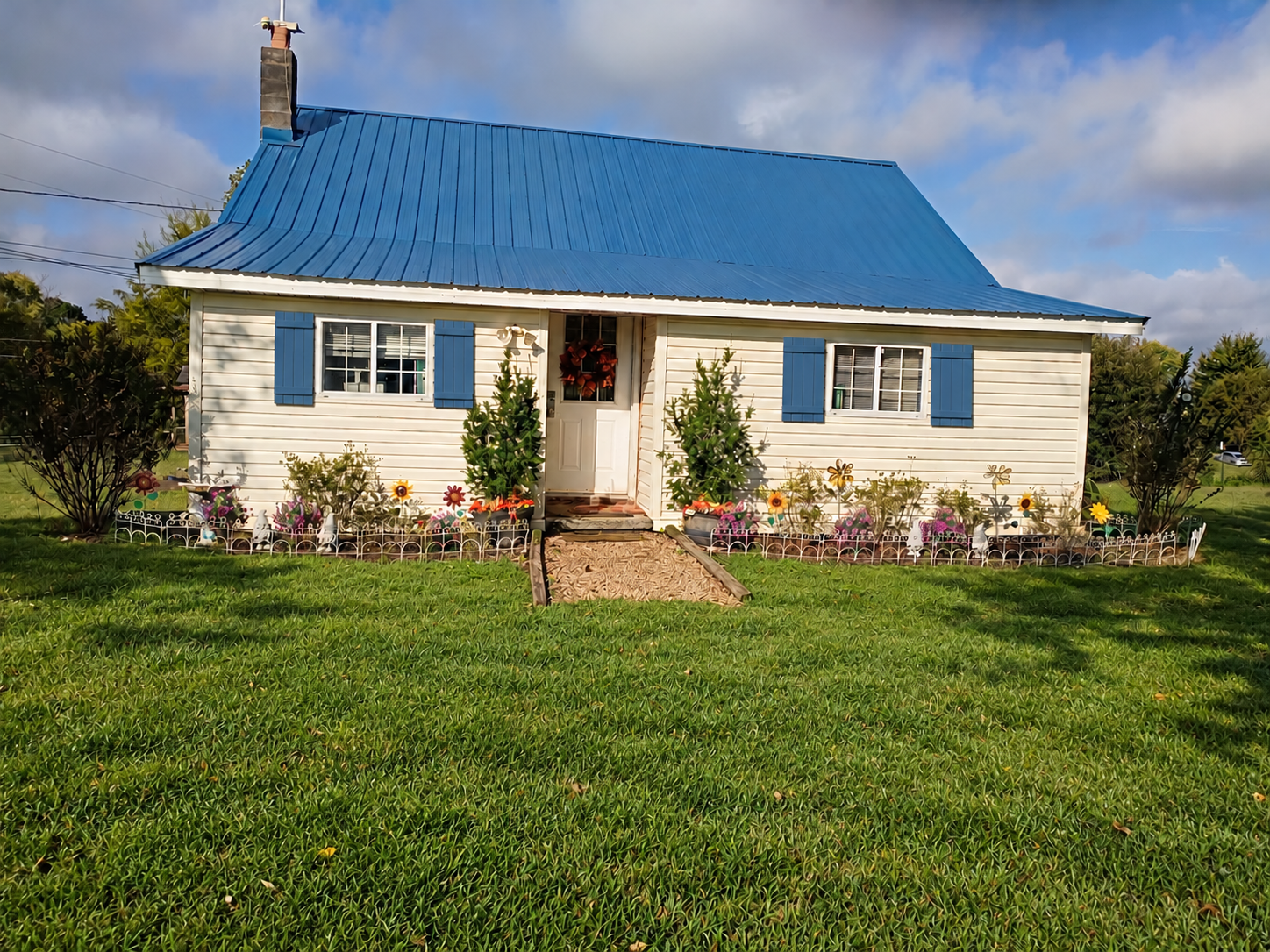 Front of the farmhouse with cameo vinyl siding, roof-matching shutters, and green lawn